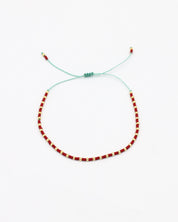An adjustable bracelet with gold and red beads and rhinestones on a white background.