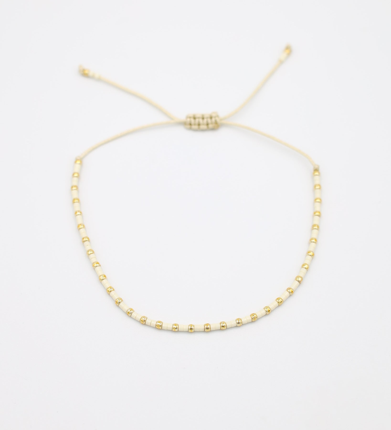 Flat-lay image of the Anya bracelet in a white and gold bead combination, featuring an adjustable sliding closure made of matching cream-colored cord.