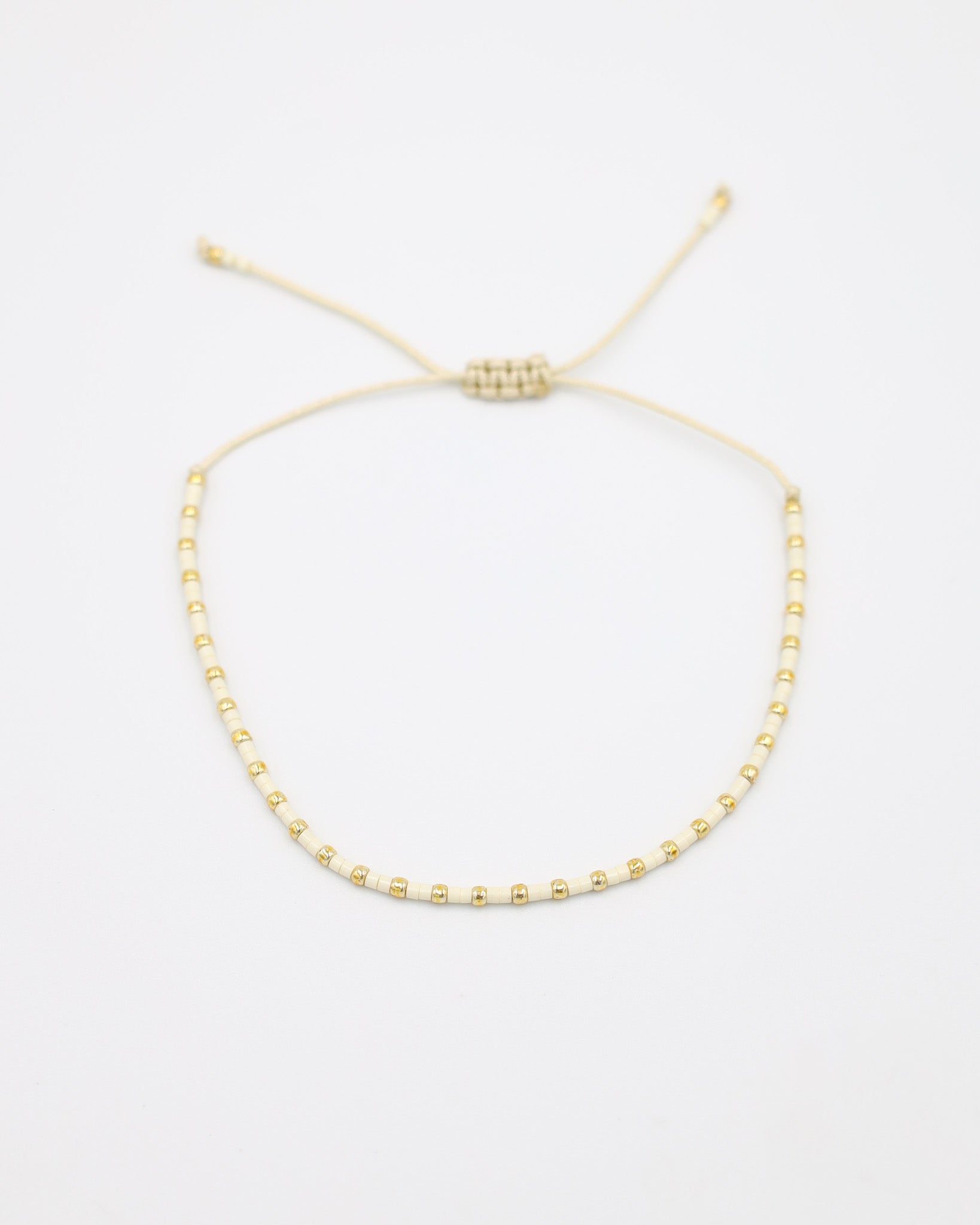 Flat-lay image of the Anya bracelet in a white and gold bead combination, featuring an adjustable sliding closure made of matching cream-colored cord.