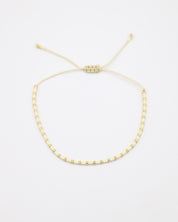 Flat-lay image of the Anya bracelet in a white and gold bead combination, featuring an adjustable sliding closure made of matching cream-colored cord.