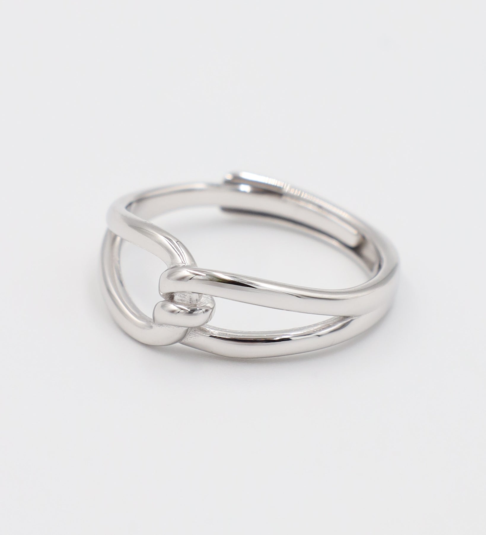 A simple silver ring with a unique design, featuring a knot-like pattern on a white background.