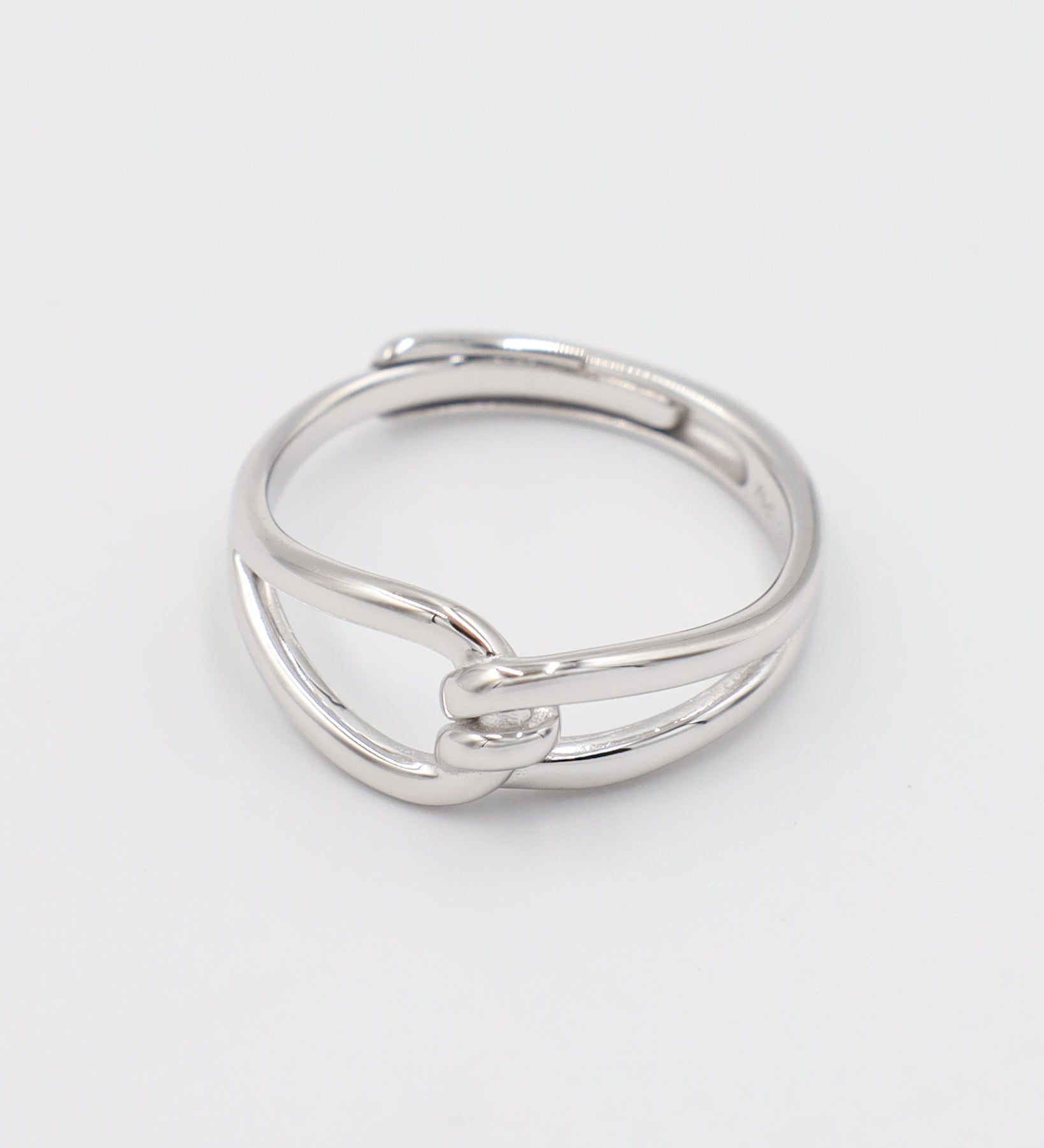 A simple silver ring with a unique design, featuring a knot-like pattern on a white background.