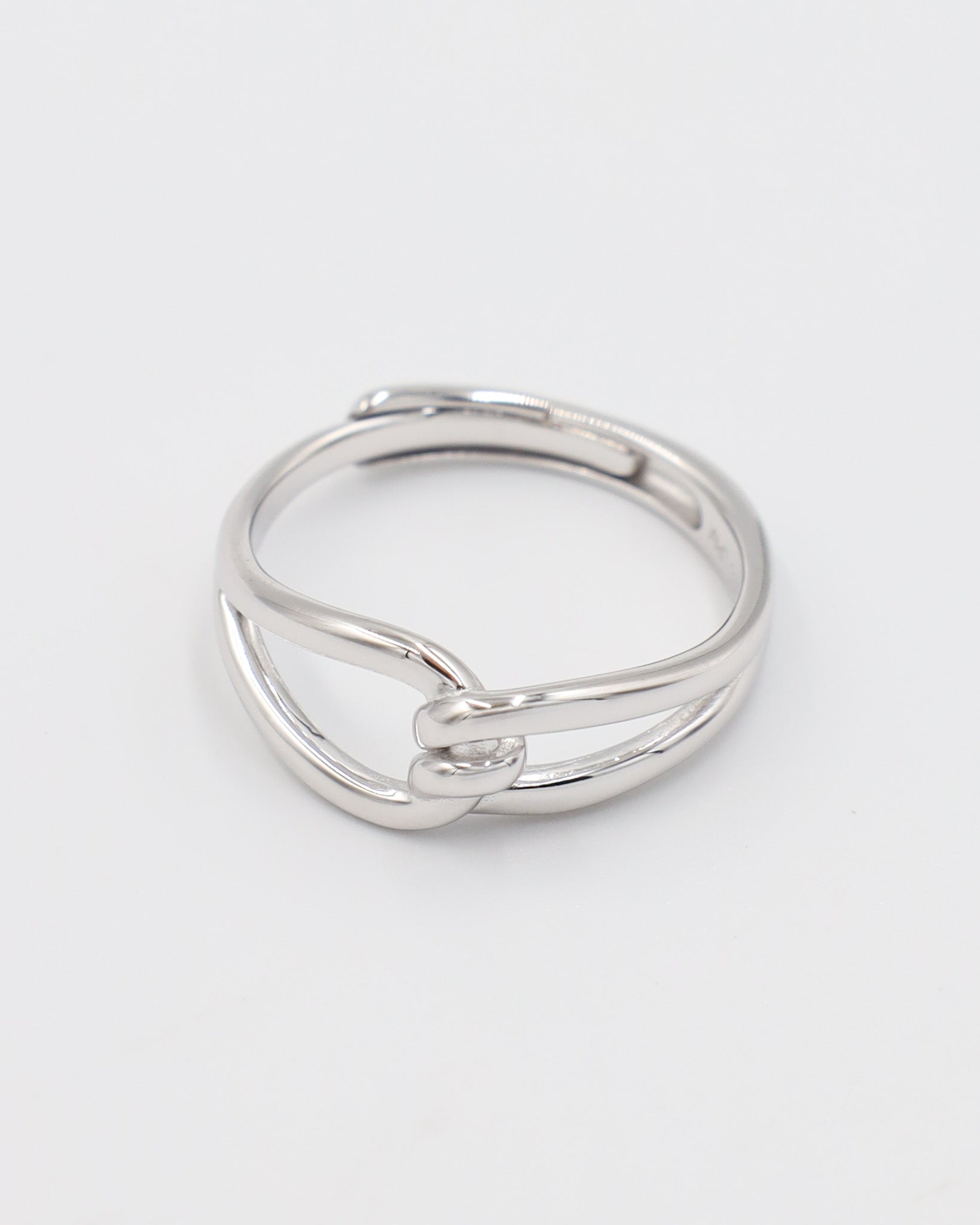 A simple silver ring with a unique design, featuring a knot-like pattern on a white background.