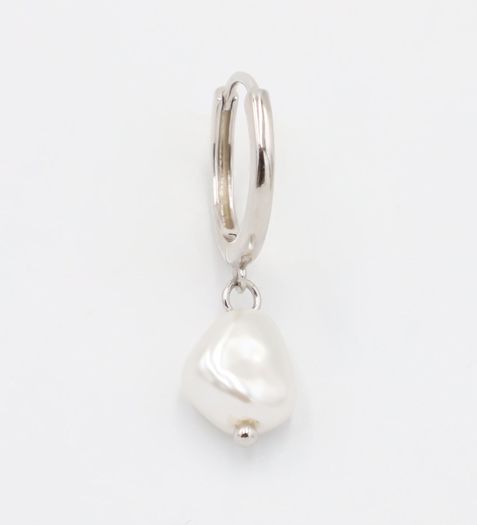 A silver-colored hoop earring with a white pearl charm attached to it.