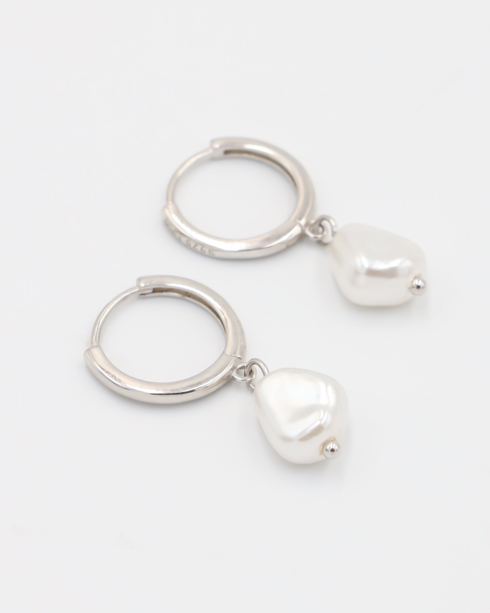 A silver-colored hoop earring with a white pearl charm attached to it.