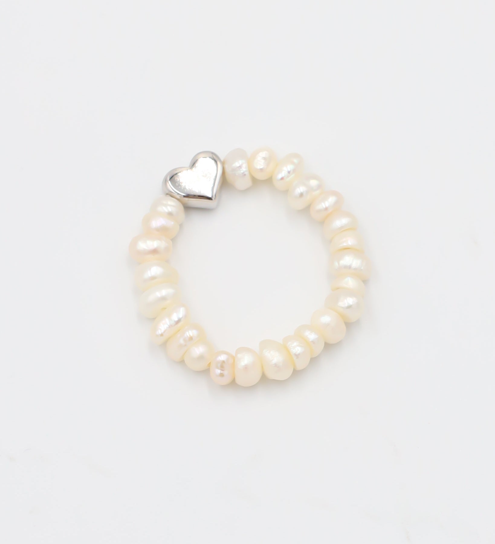 A silver ring with a heart-shaped clasp and white pearl-like beads.