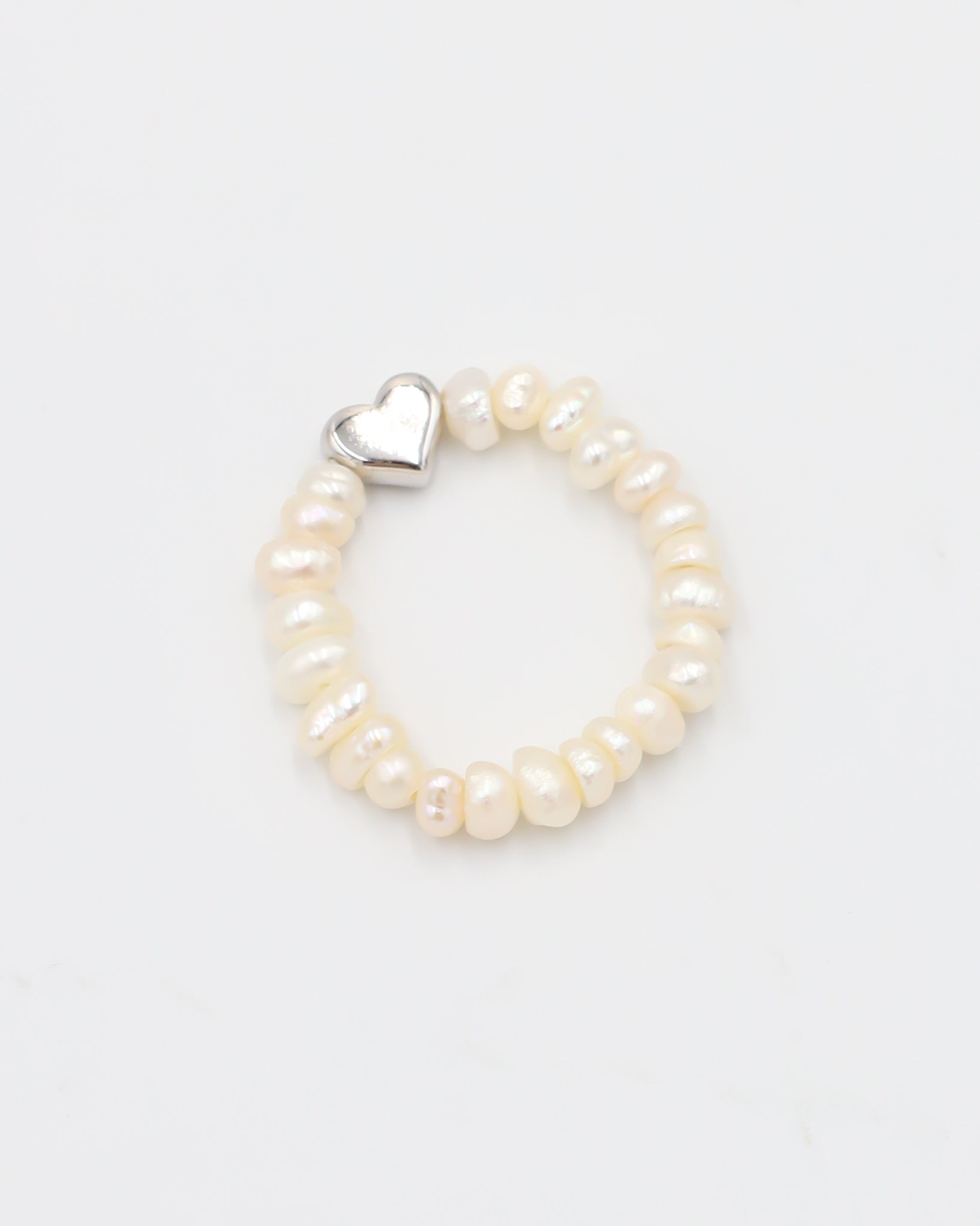 A silver ring with a heart-shaped clasp and white pearl-like beads.