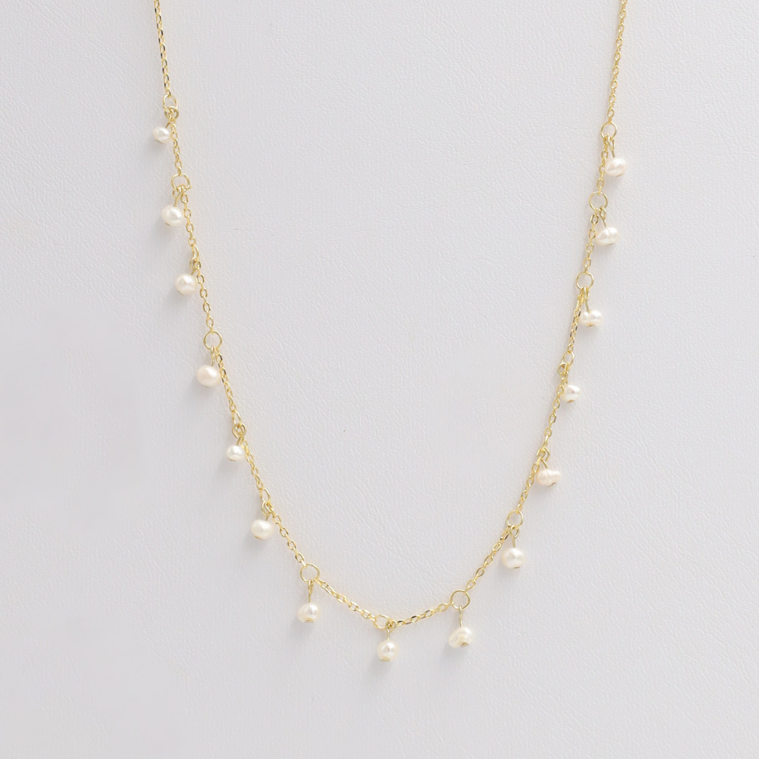 A gold-colored necklace with small pearl-like beads distributed along its length, displayed against a white background.
