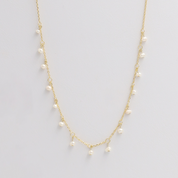 A gold-colored necklace with small pearl-like beads distributed along its length, displayed against a white background.