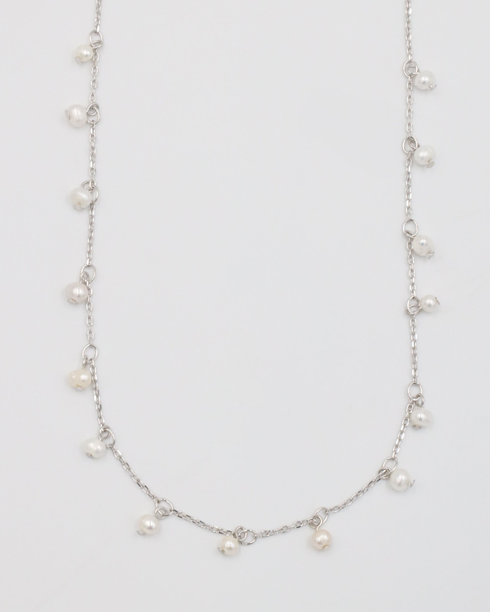 A silver necklace with a series of small pearls scattered along a chain, displayed against a white background.