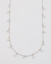 A silver necklace with a series of small pearls scattered along a chain, displayed against a white background.