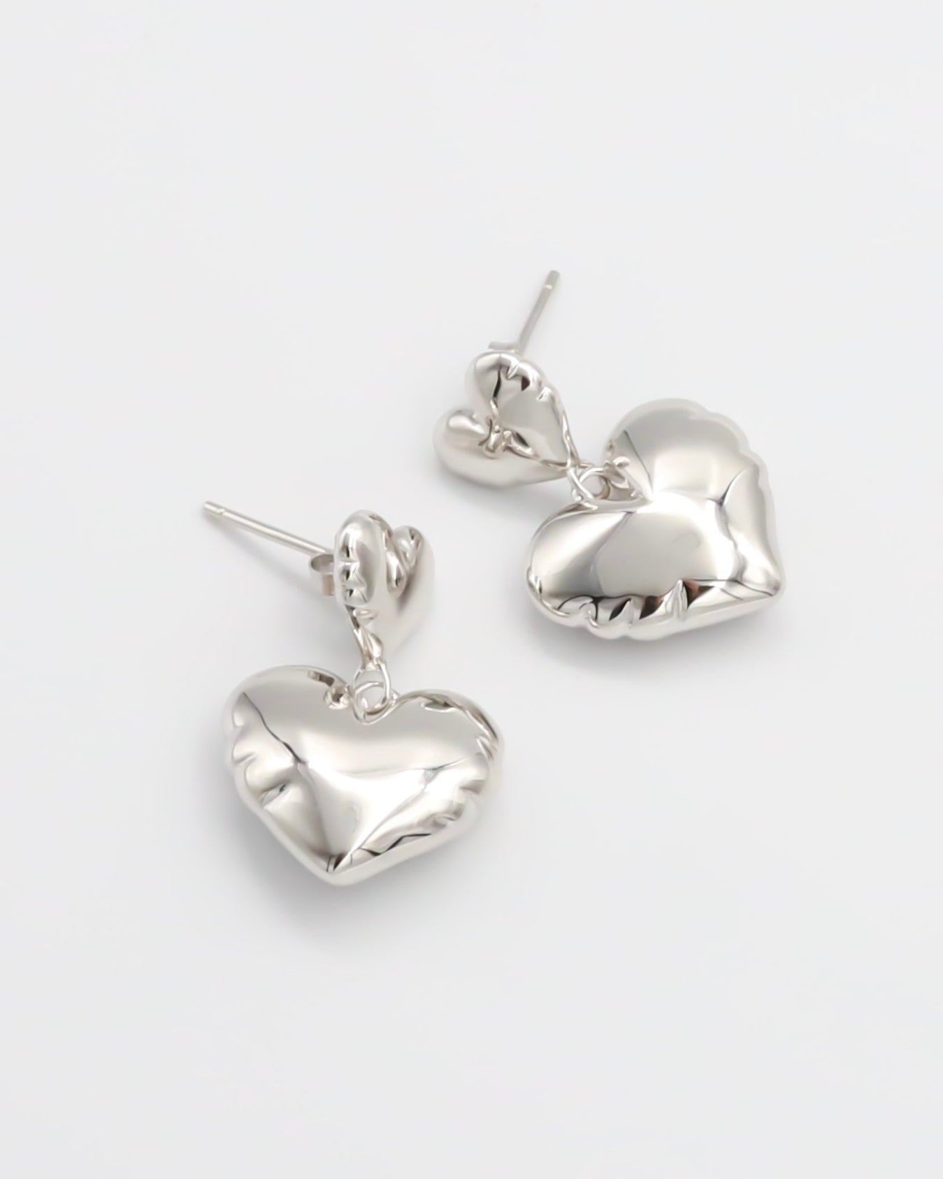 A pair of silver heart-shaped stud earrings with butterfly clasps on a white background