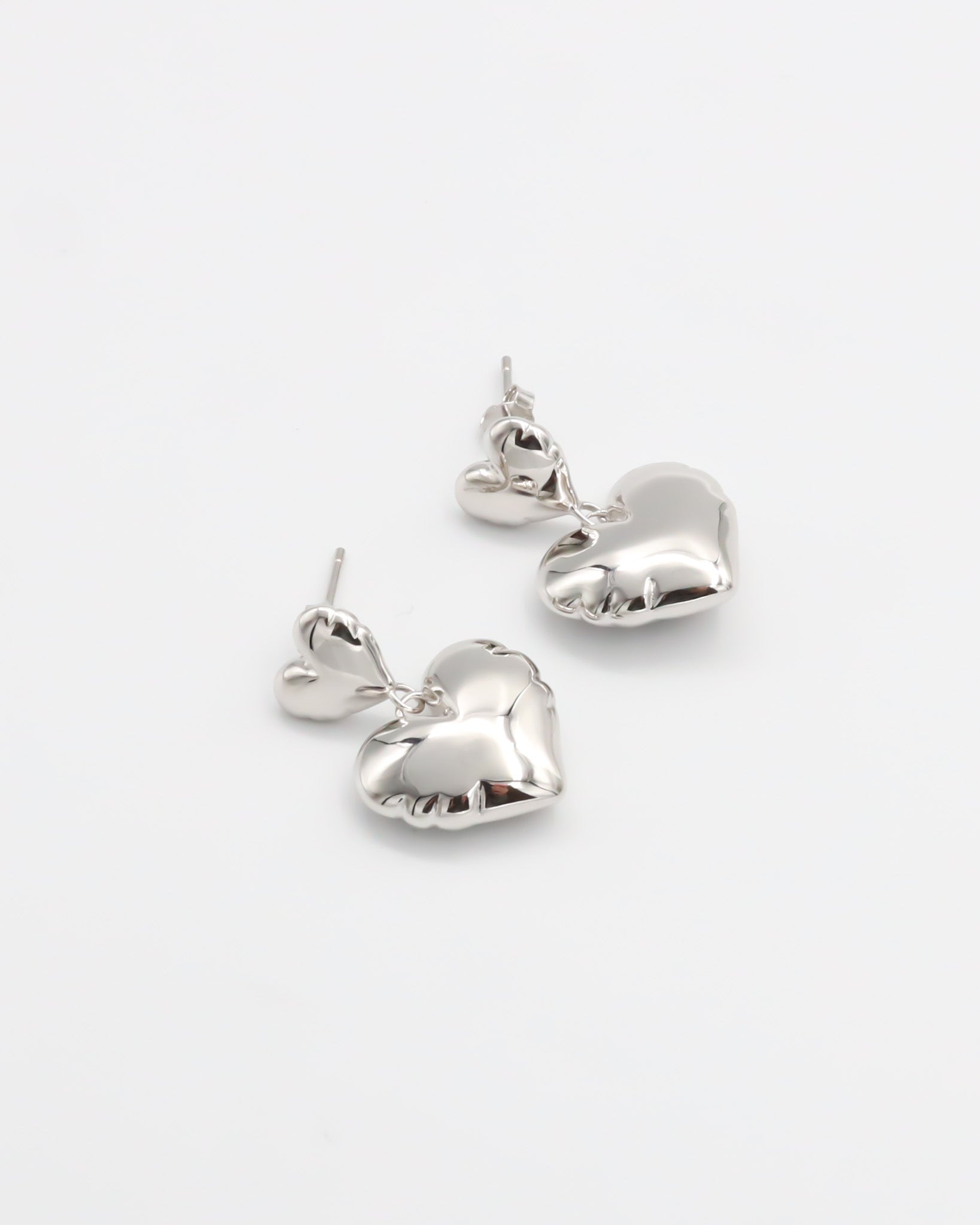 A pair of silver heart-shaped stud earrings with butterfly clasps on a white background