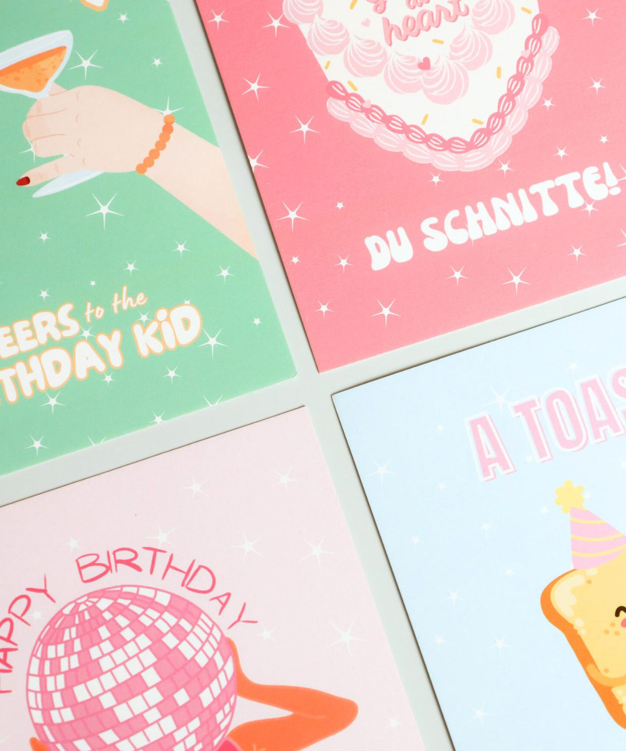 A flat lay of four colorful birthday cards with playful illustrations and text, including designs with cocktails, cake, disco ball, and toast – part of ruru. studios’ birthday card collection.