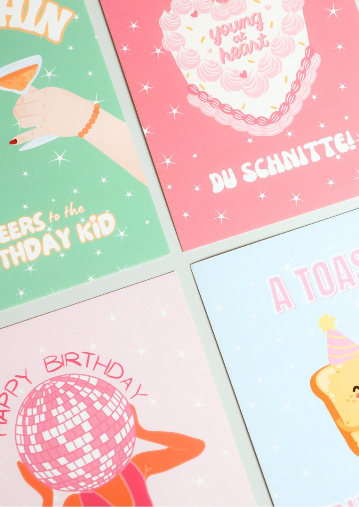 A flat lay of four colorful birthday cards with playful illustrations and text, including designs with cocktails, cake, disco ball, and toast – part of ruru. studios’ birthday card collection.