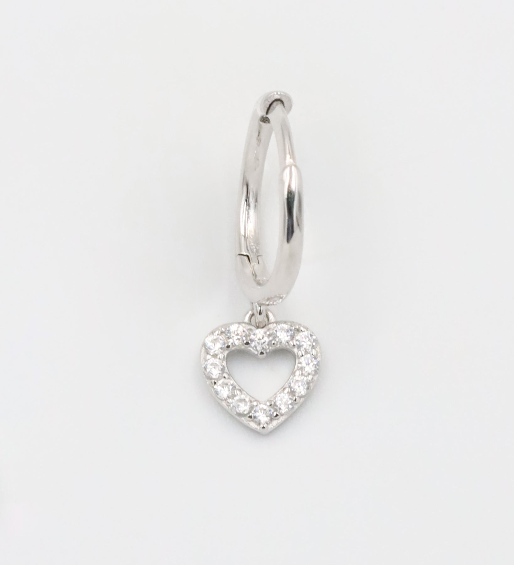 A silver hoop earring with a heart-shaped charm hanging from it, displayed against a white background.