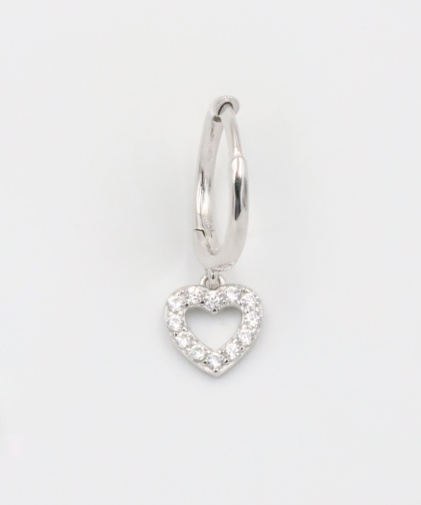 A silver hoop earring with a heart-shaped charm hanging from it, displayed against a white background.