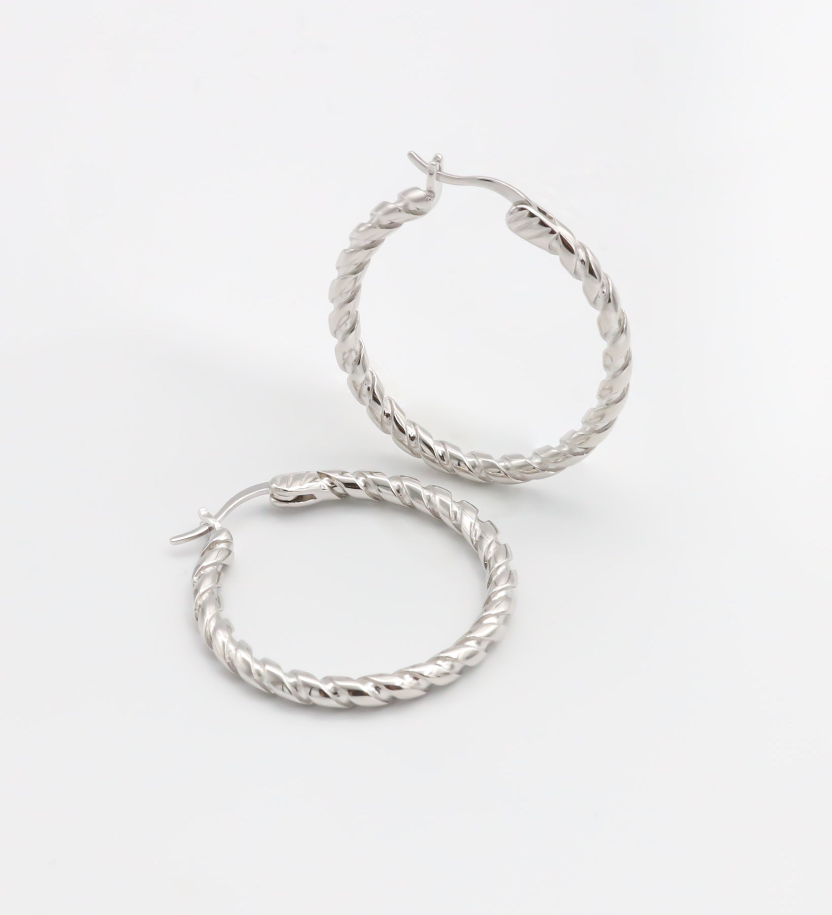 A pair of silver hoop earrings with a twist pattern on a white background