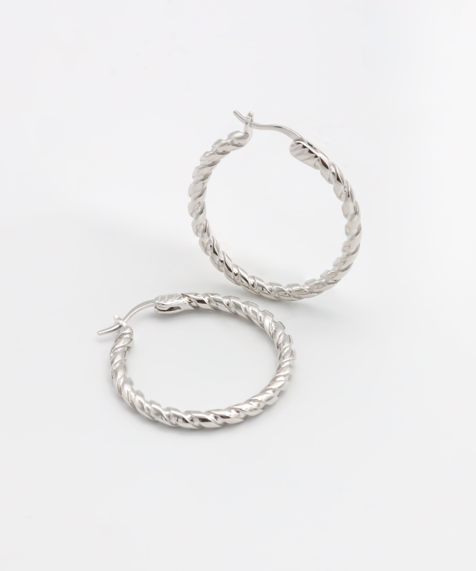 A pair of silver hoop earrings with a twist pattern on a white background