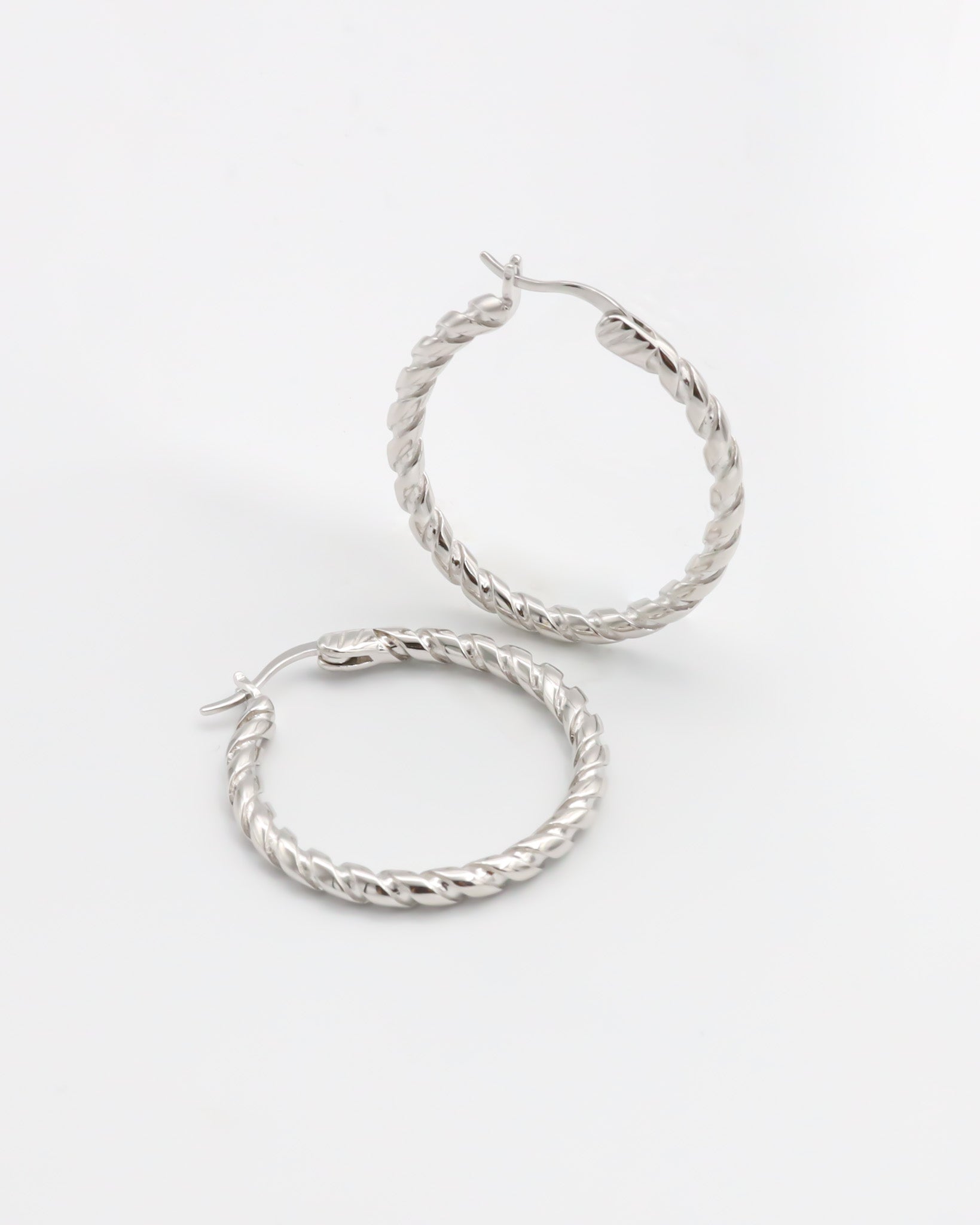 A pair of silver hoop earrings with a twist pattern on a white background