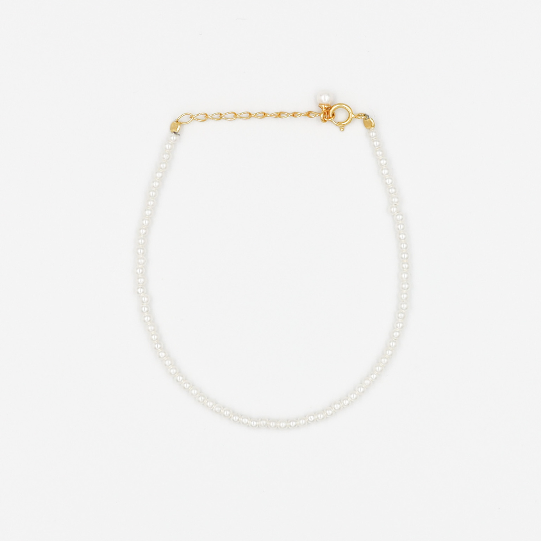 A gold-colored necklace featuring a series of size small pearl beads and a small gold chain.