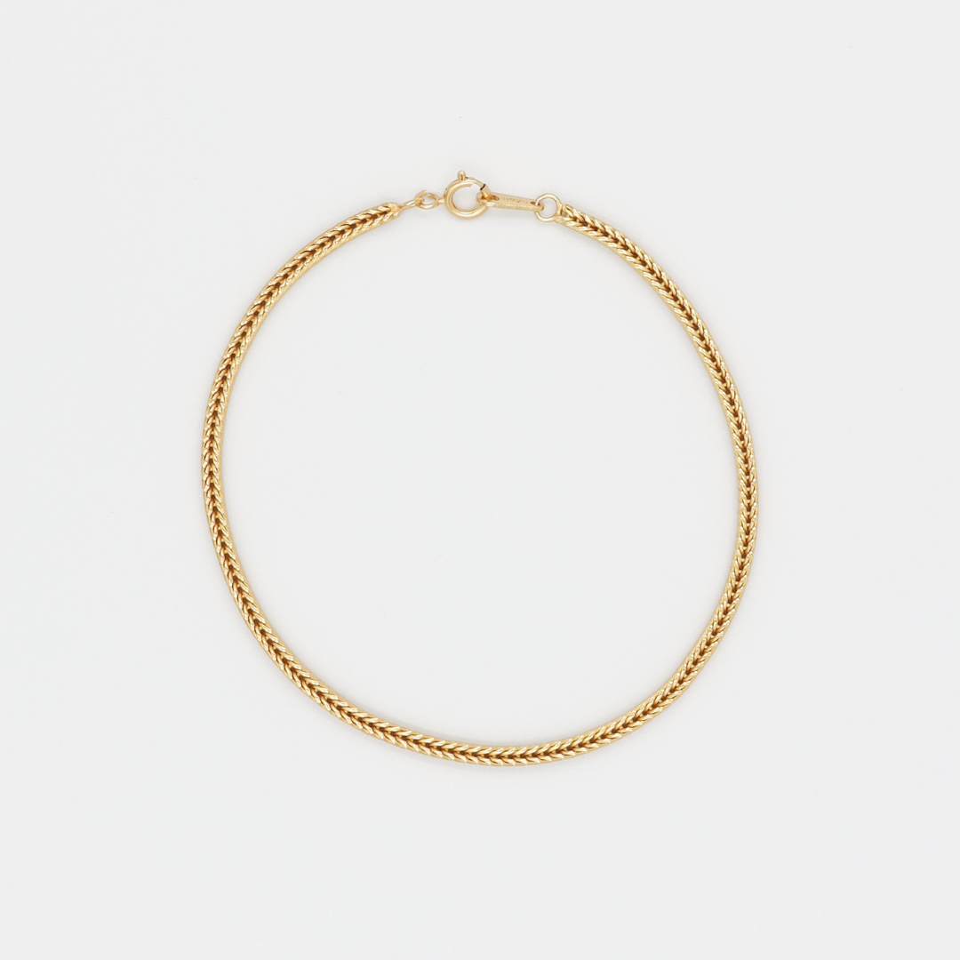 A gold-colored necklace laid out on a plain background.