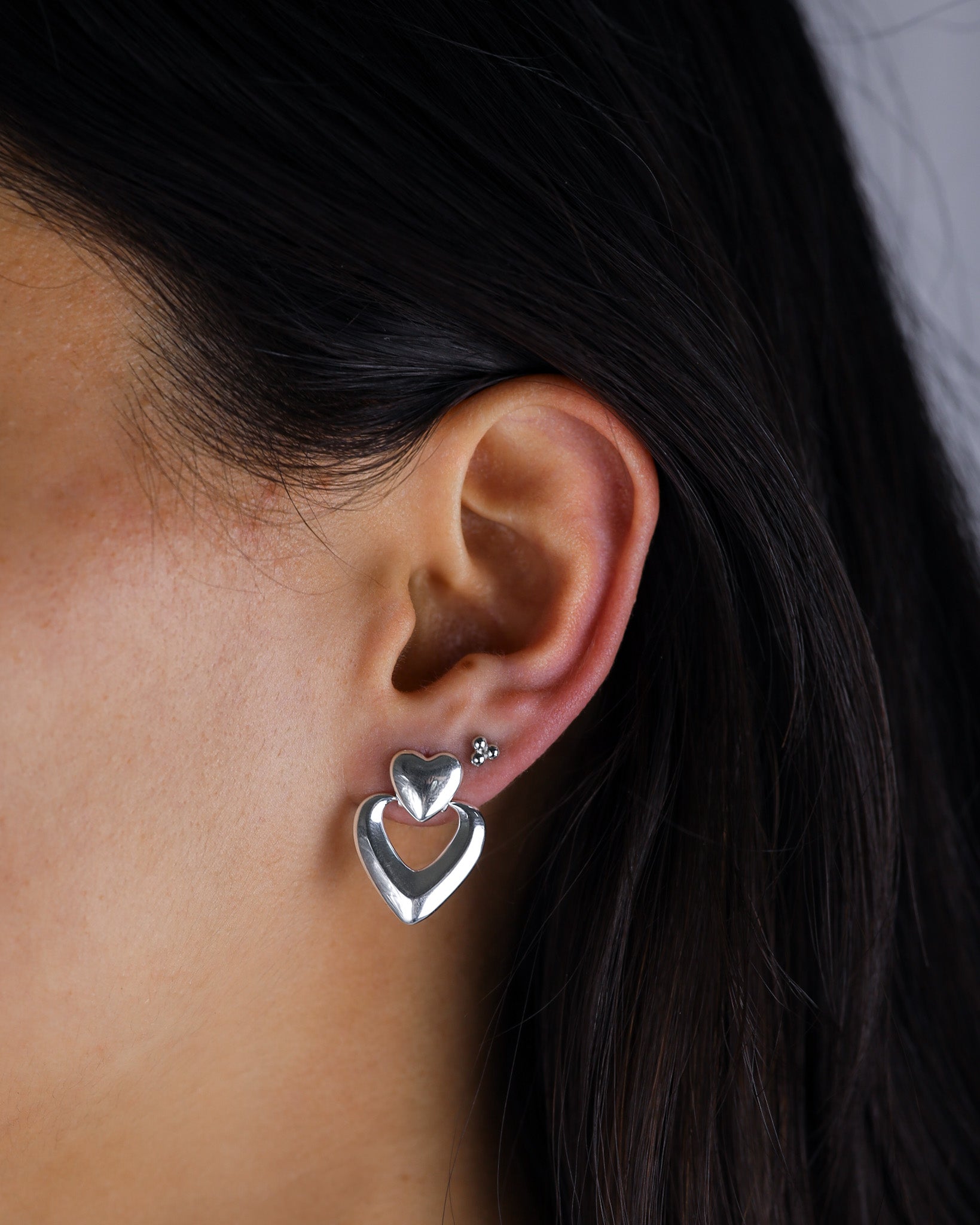 Close-up of an ear wearing a silver heart-shaped earring with a blurred background