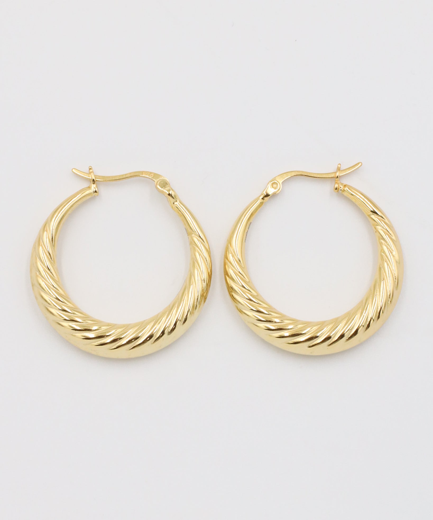 A pair of gold-colored hoop earrings with a latch back clasp on a white background.