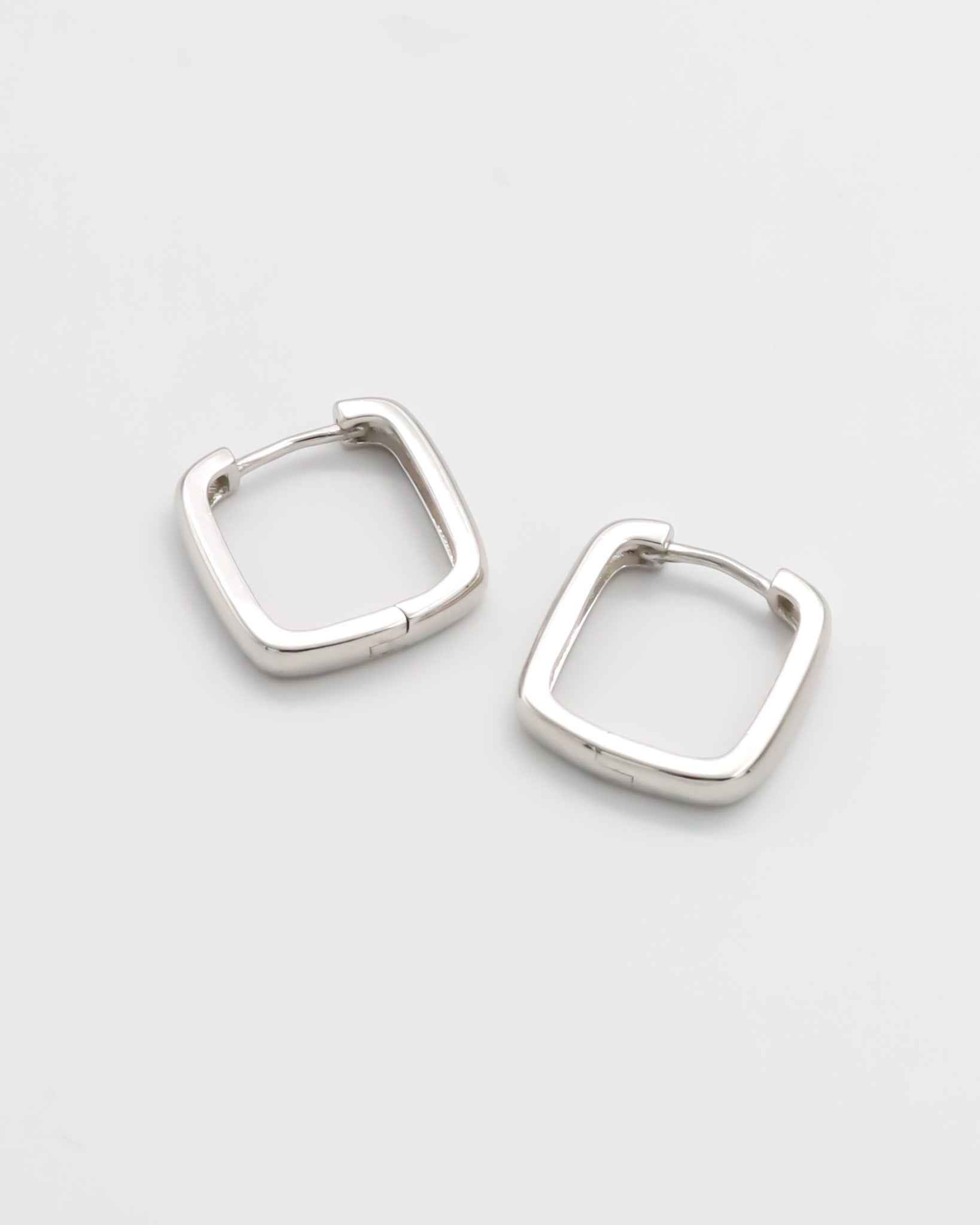 A pair of silver-colored hoop earrings with a hinged clasp, displayed against a white background.