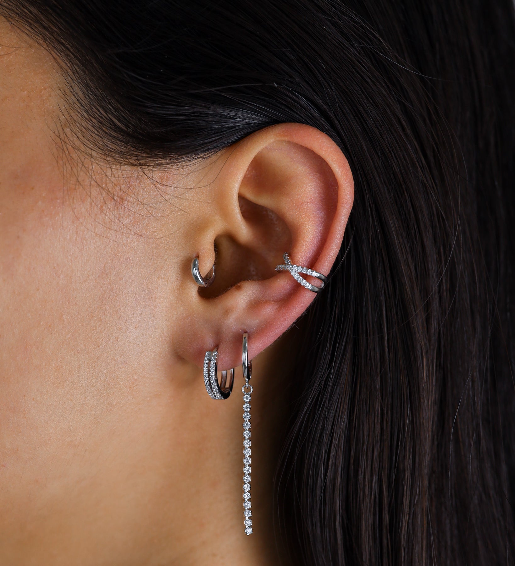 Close-up of an ear with multiple silver earrings against a dark background