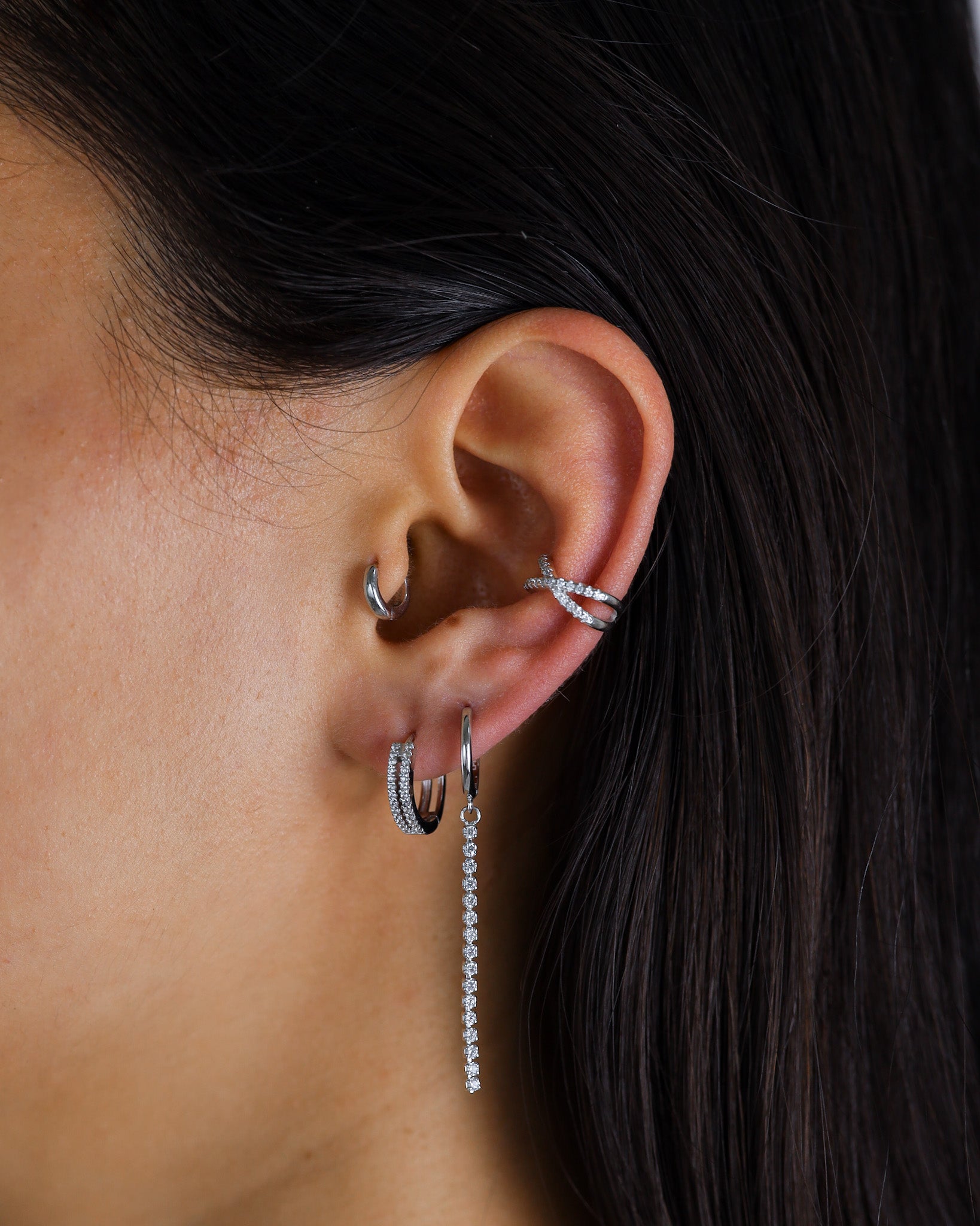 Close-up of an ear with multiple silver earrings against a dark background