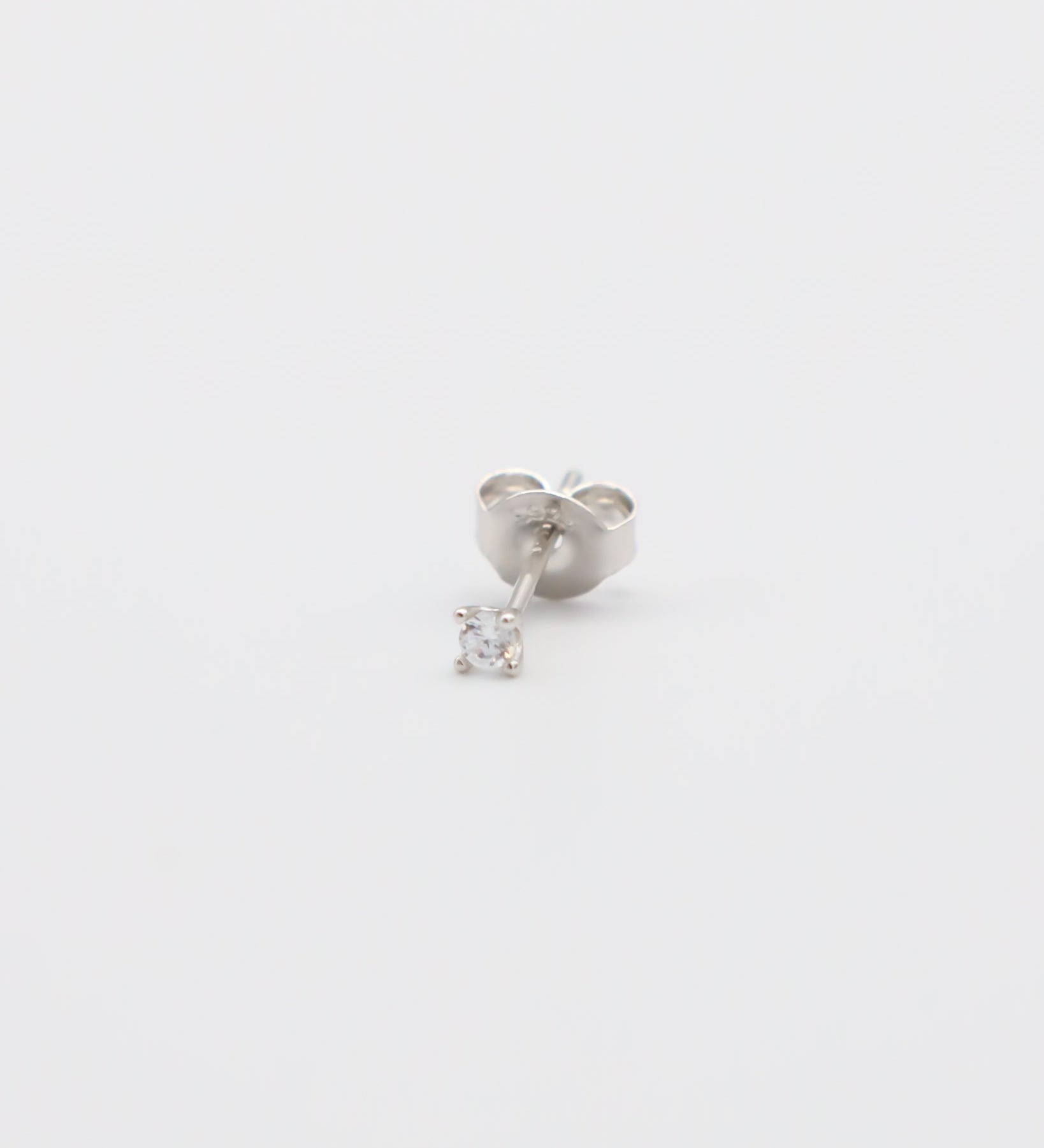A single silver stud earring with a small clear gemstone, displayed against a white background.
