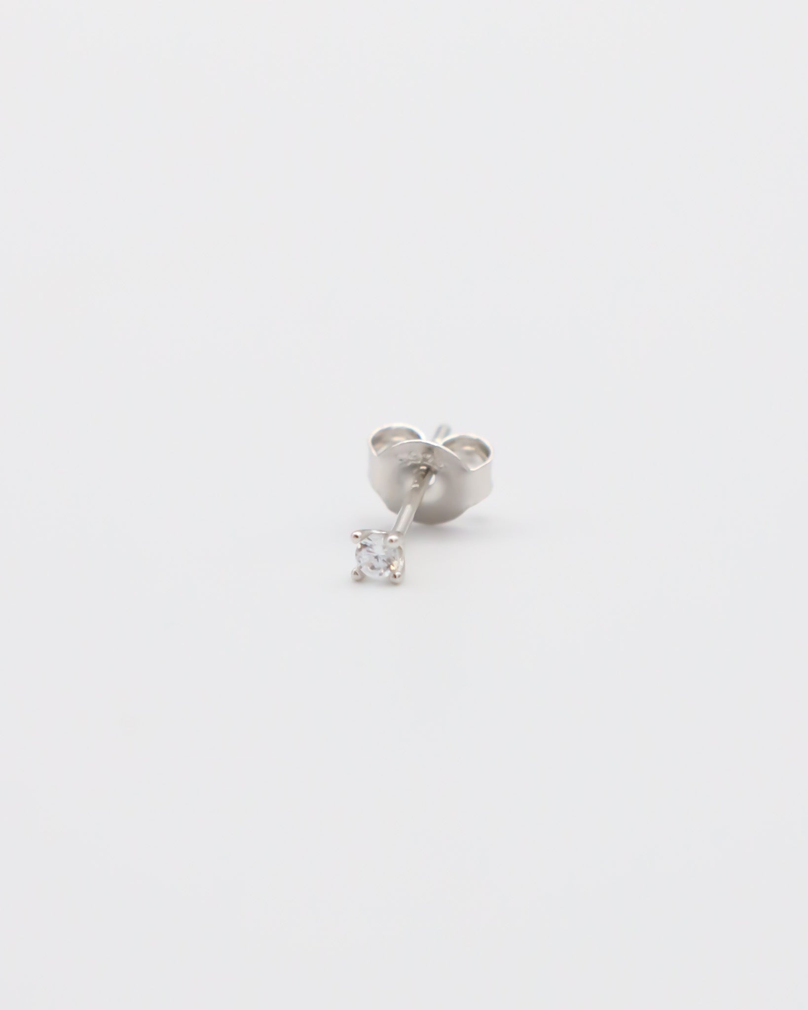 A single silver stud earring with a small clear gemstone, displayed against a white background.