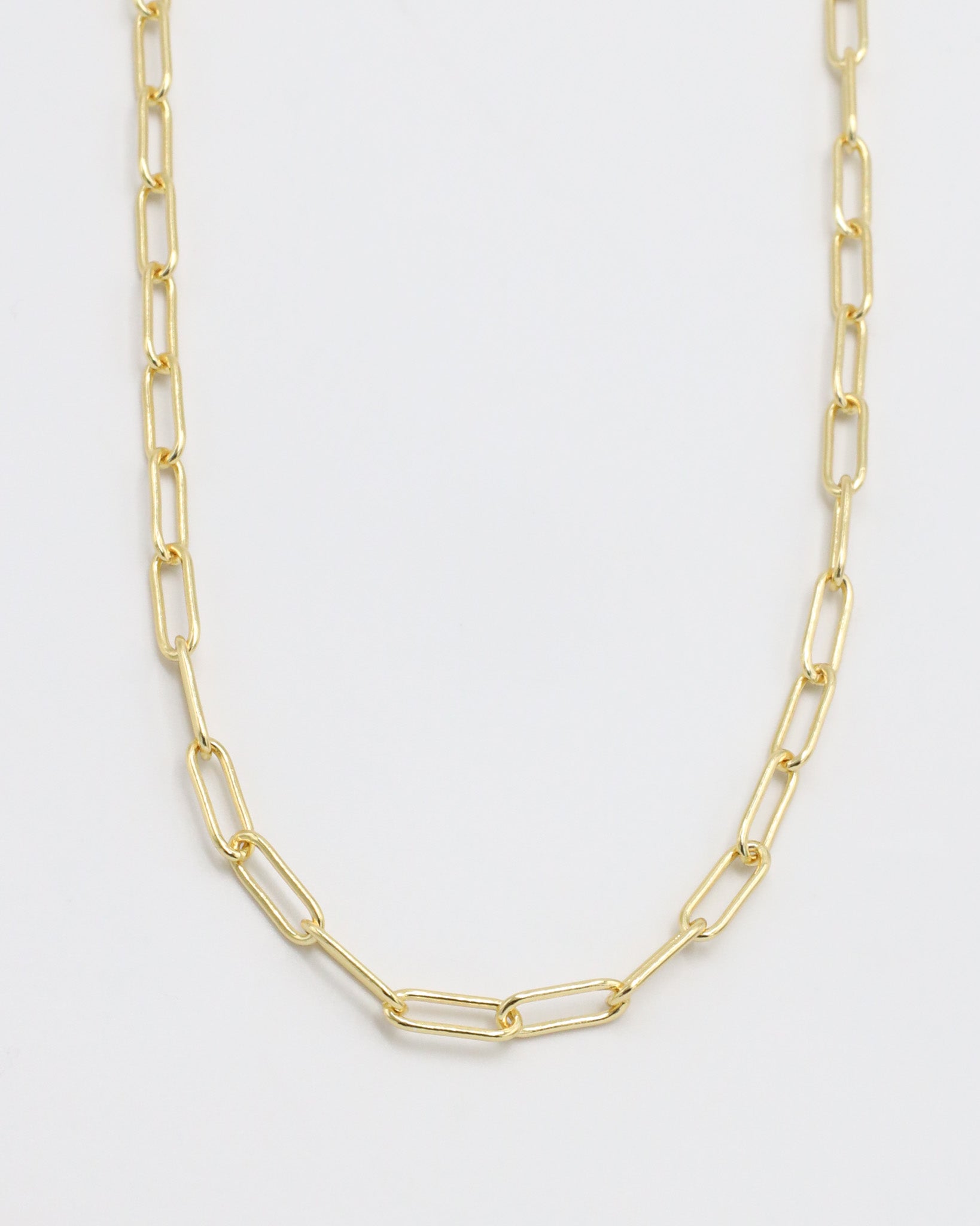 A gold-colored necklace with a chain link design, laid out on a plain background.