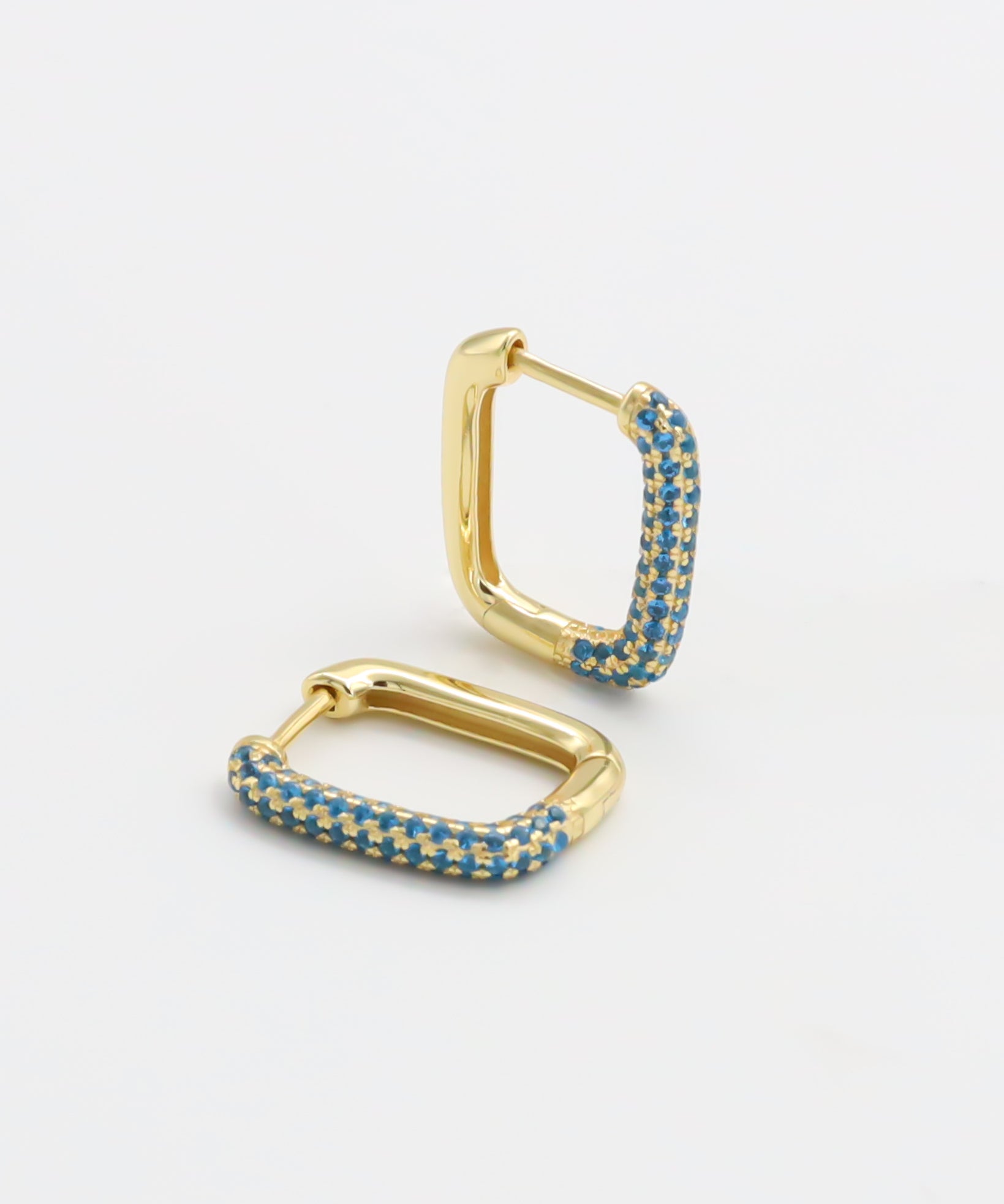 A single gold-colored hoop earring with blue gemstones set in its structure, displayed against a white background.