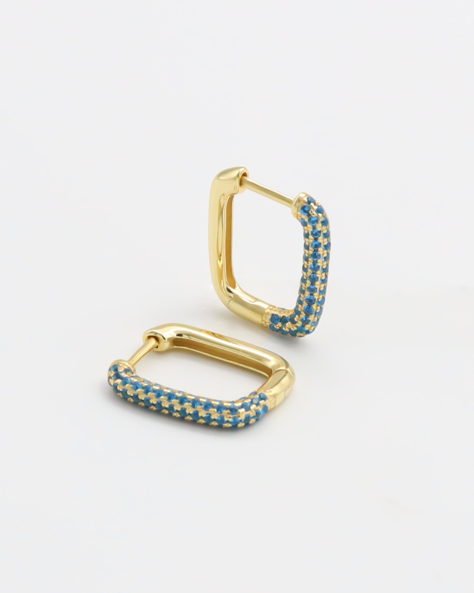 A single gold-colored hoop earring with blue gemstones set in its structure, displayed against a white background.