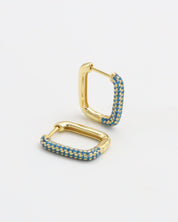 A single gold-colored hoop earring with blue gemstones set in its structure, displayed against a white background.