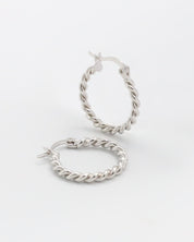 A pair of silver hoop earrings with a twist pattern and latch back clasps on a white background.
