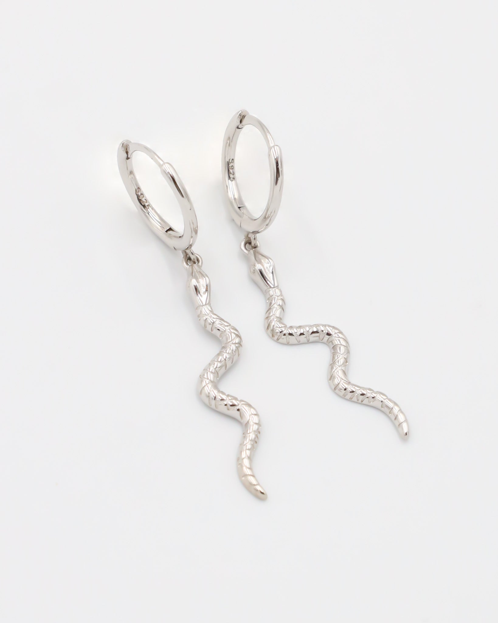 A silver hoop earring with a small silver charm shaped like a snake dangling from it.
