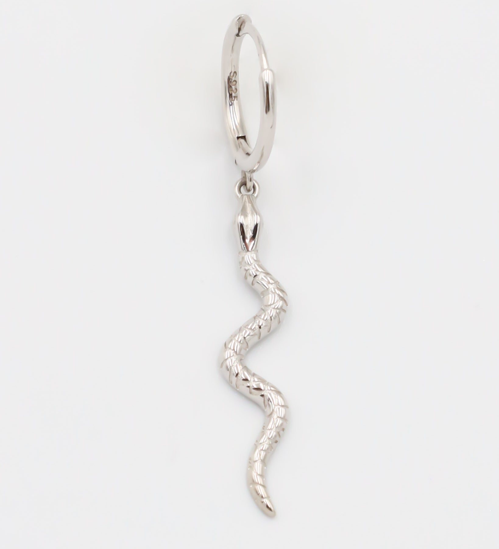 A silver hoop earring with a small silver charm shaped like a snake dangling from it.