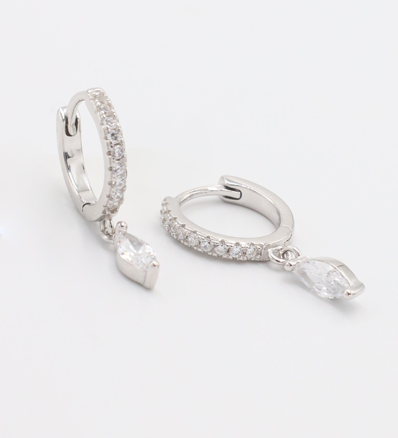 A silver hoop earring with a hinged clasp, decorated with small white gemstones along its length, displayed against a white background.