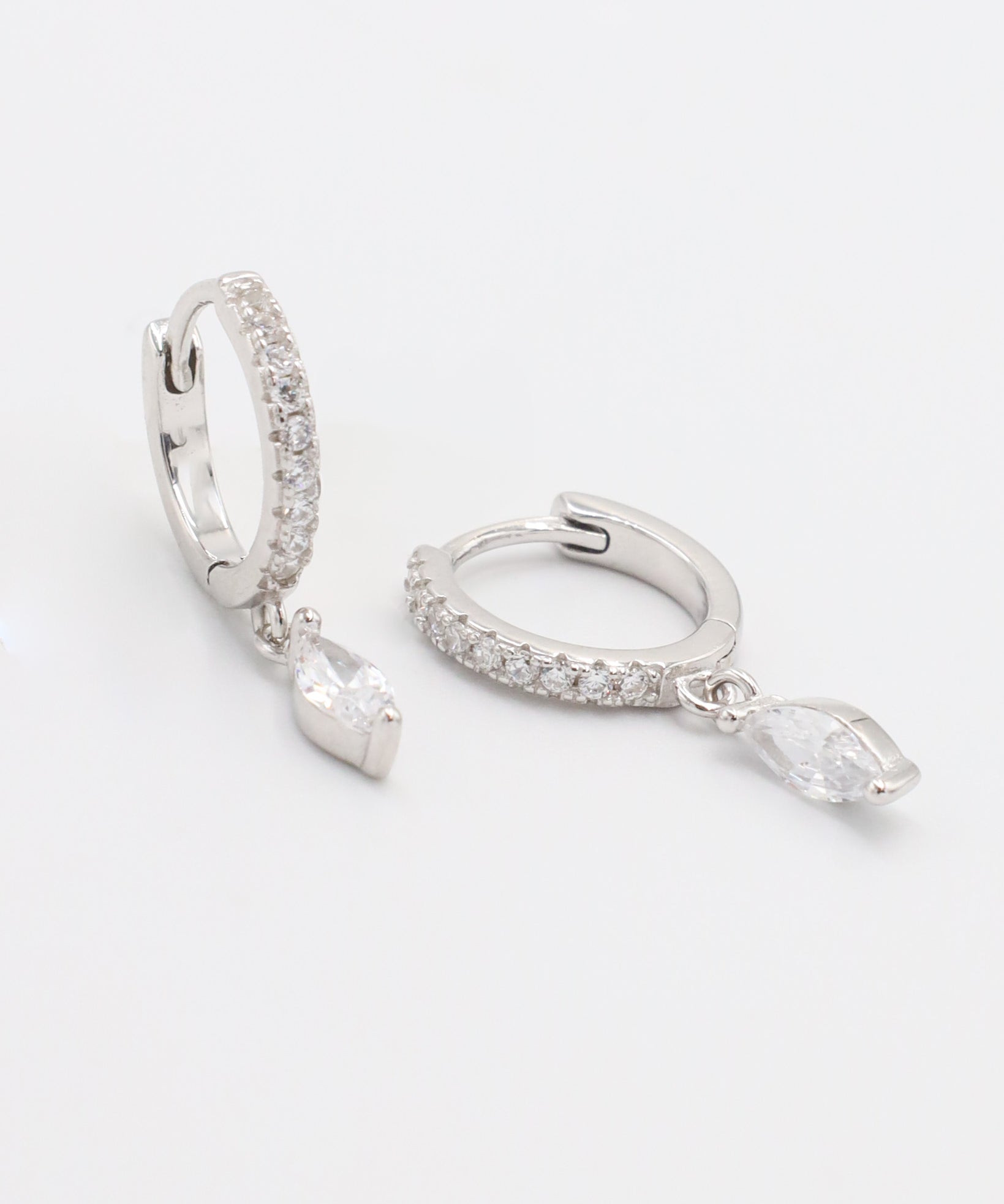 A silver hoop earring with a hinged clasp, decorated with small white gemstones along its length, displayed against a white background.