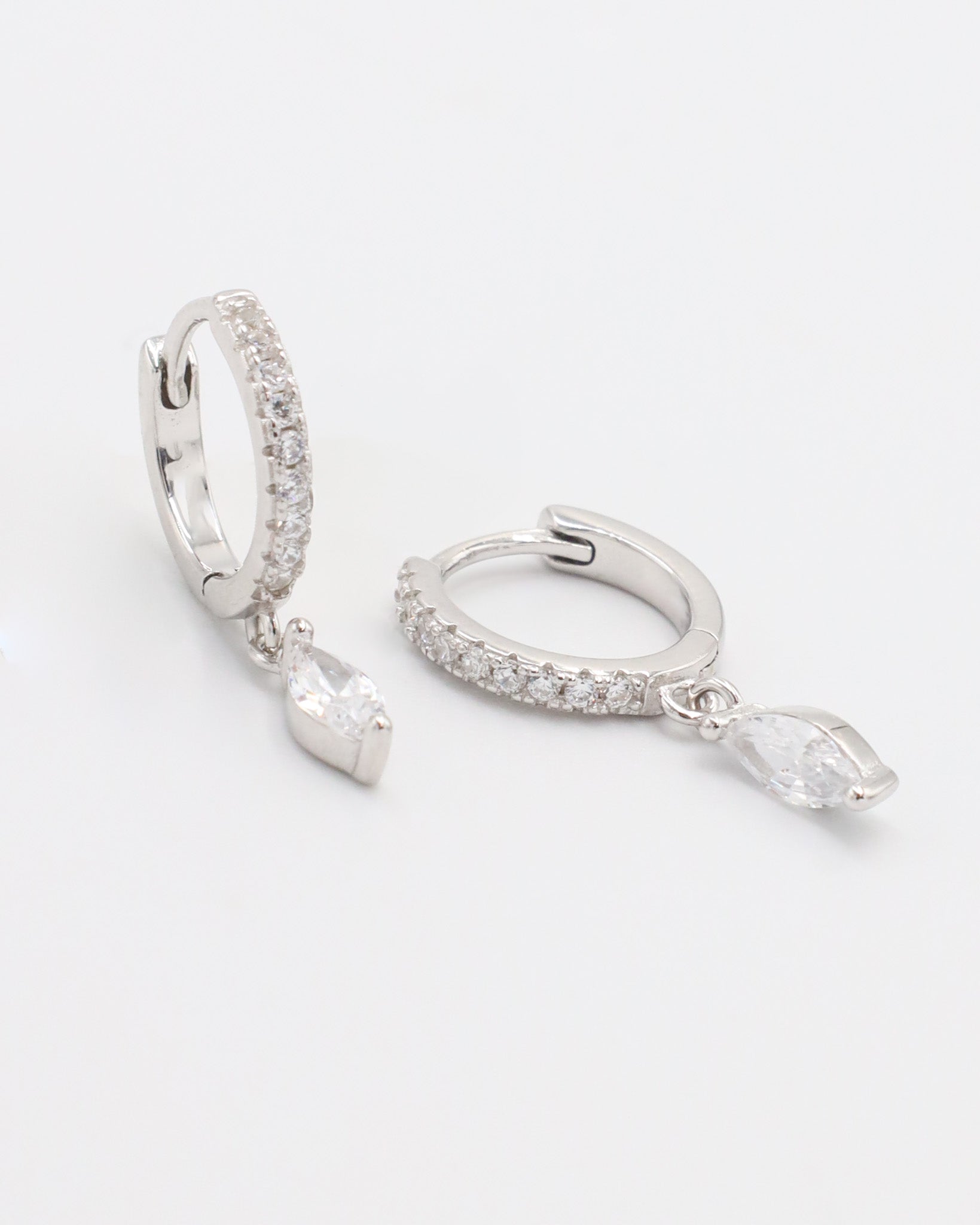 A silver hoop earring with a hinged clasp, decorated with small white gemstones along its length, displayed against a white background.