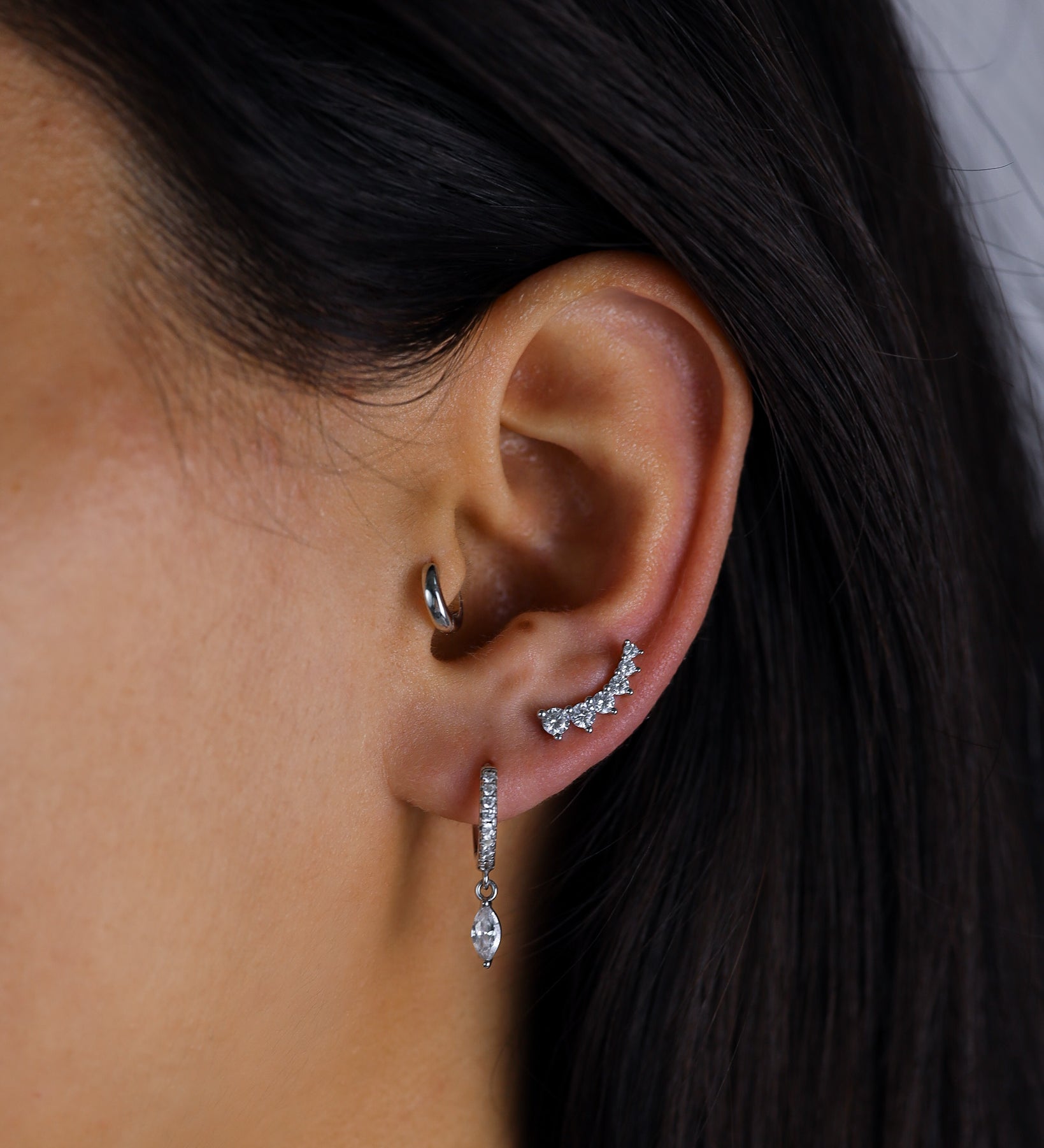 Close-up of an ear wearing a silver hoop earring and a dangling earring with a dark background.