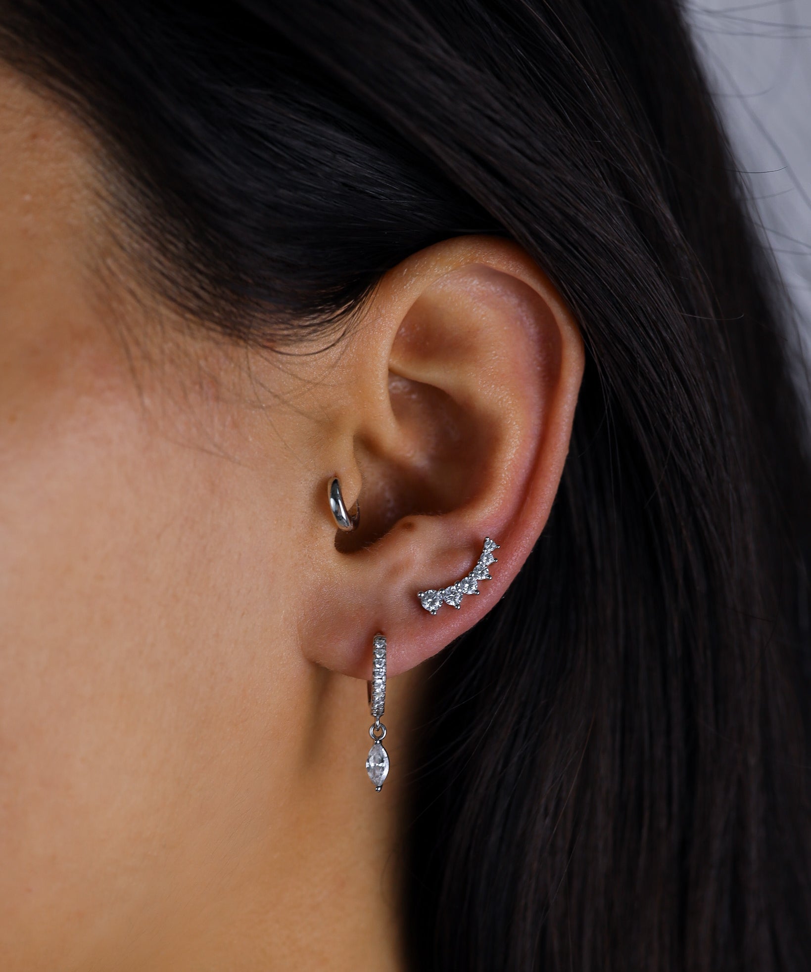 Close-up of an ear wearing a silver hoop earring and a dangling earring with a dark background.