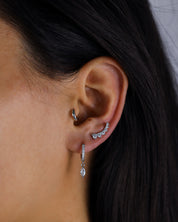 Close-up of an ear wearing a silver hoop earring and a dangling earring with a dark background.