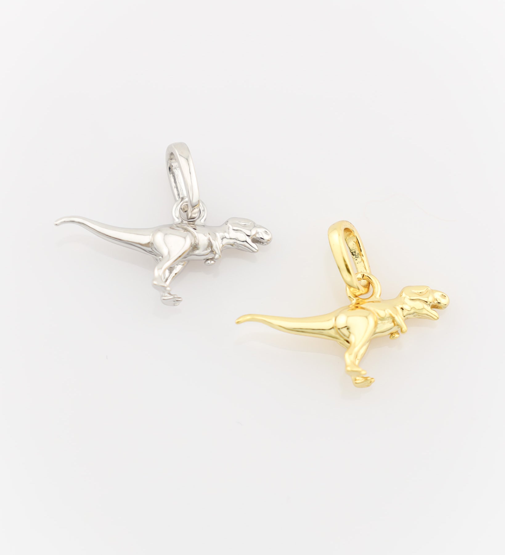 Silver and gold dinosaur-shaped pendants on a white background