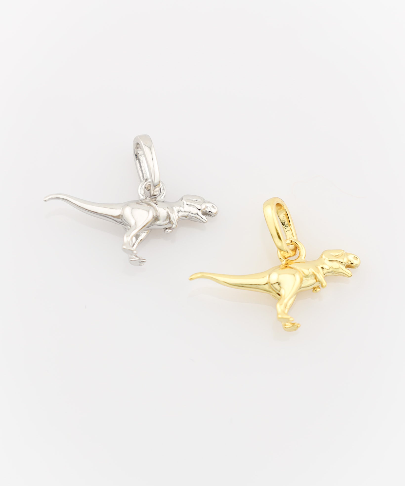 Silver and gold dinosaur-shaped pendants on a white background