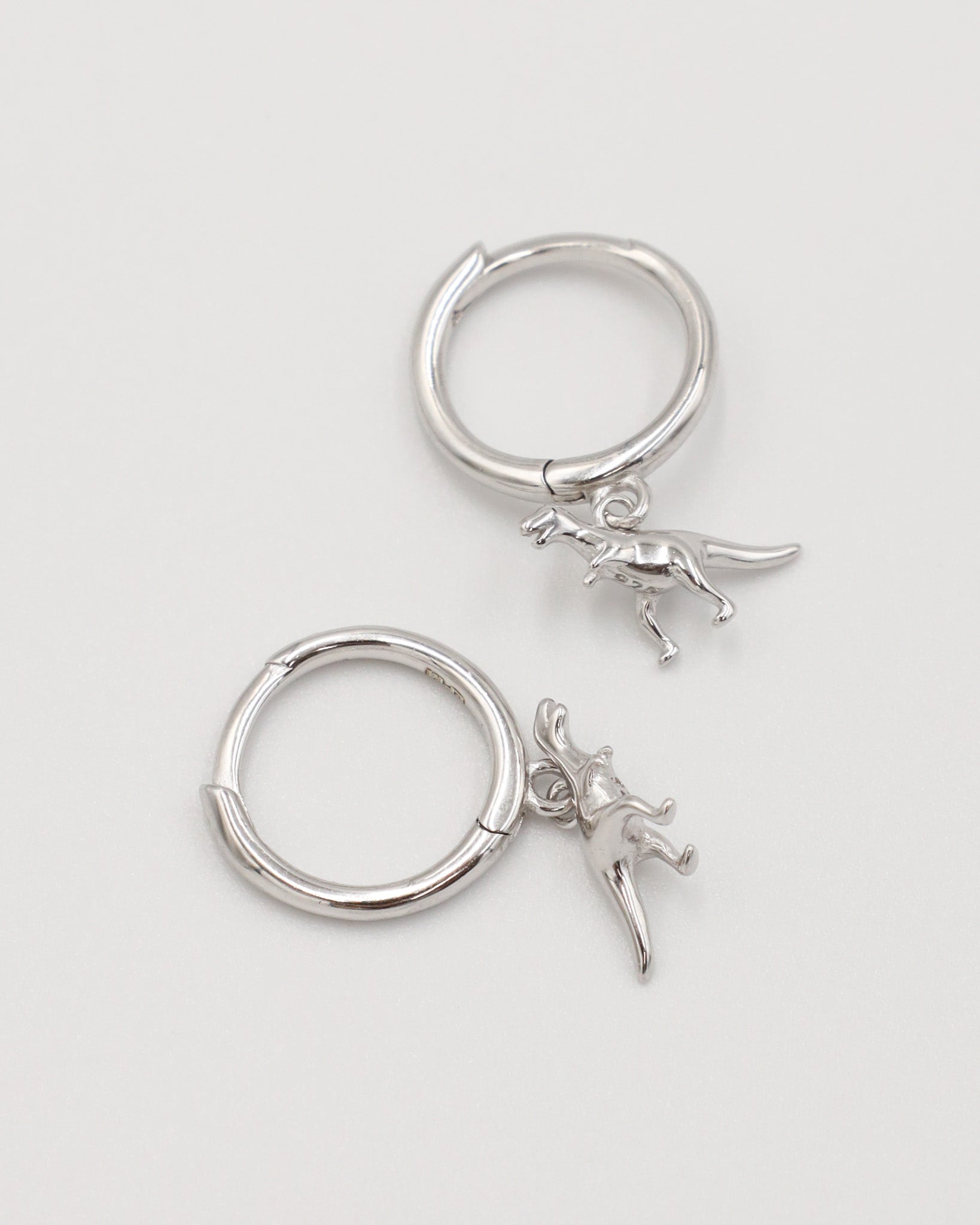 A silver-colored hoop earring with a small dinosaur charm attached to it.