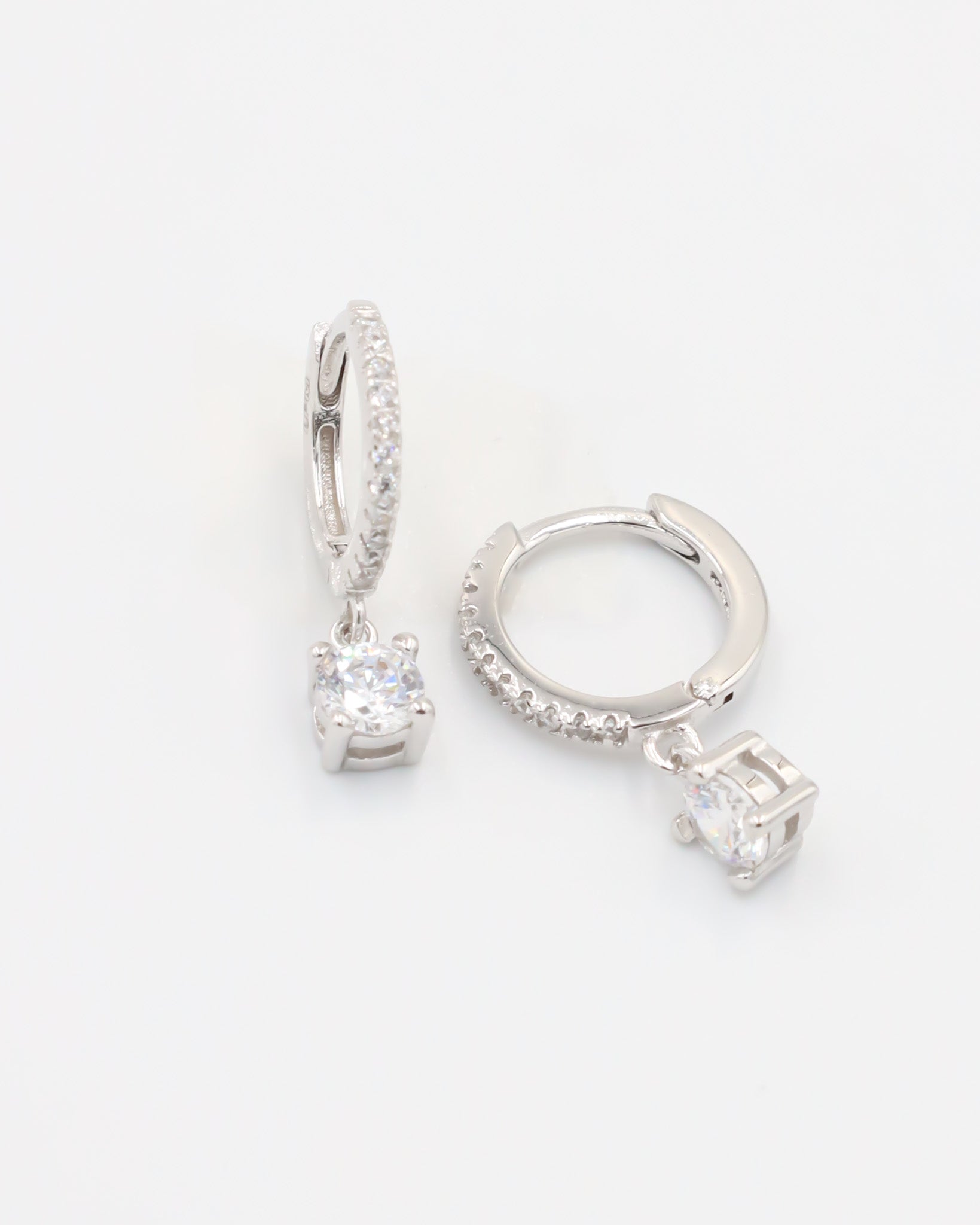 A silver hoop earring with a hinged clasp and a central gemstone, possibly a diamond, surrounded by smaller stones.
